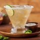 Margarita cocktail on plate with jalapeno slices and a bowl of salt